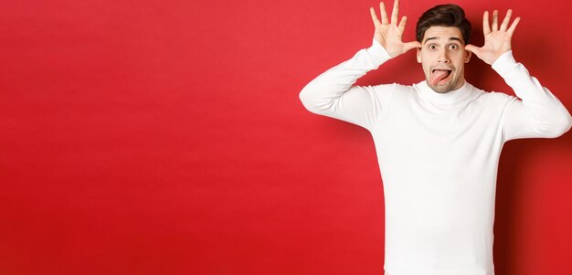 Portrait d'un drôle de type caucasien montrant la langue et faisant des grimaces portant un pull blanc debout à nouveau...