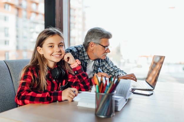 Portrait du grand-père et de la petite-fille faisant leurs devoirs avec un ordinateur portable et des livres