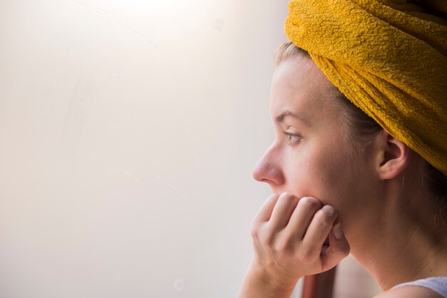 Portrait du profil d&#39;une jeune femme assise seule regardant la fenêtre. Entrez la fille près de la fenêtre en train de penser à quelque chose.