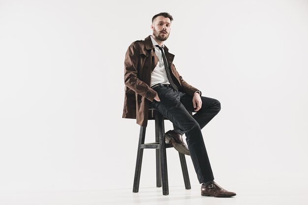 Portrait d'élégant beau jeune homme assis au studio contre le blanc. Homme, porter, veste