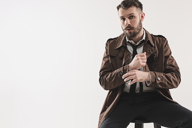 Portrait d'élégant beau jeune homme assis au studio contre le blanc.