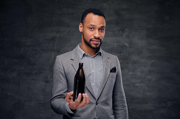 Portrait d'un élégant homme noir américain vêtu d'un costume gris tenant une bouteille de bière artisanale.