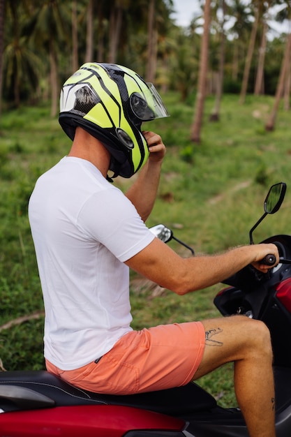 Portrait de l'élégant touriste masculin tatoué en lunettes de soleil, casque et chemise ouverte bleue sur moto