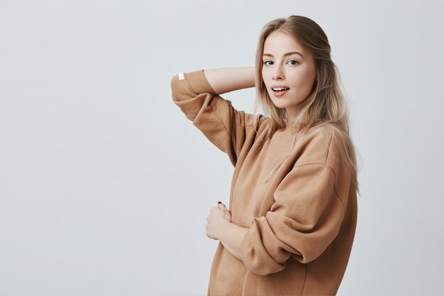 Portrait de l'élégante belle séduisante jeune femme européenne aux yeux noirs et longs cheveux blonds posant à l'intérieur. Modèle féminin branché isolé