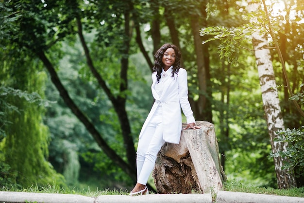 Portrait d'élégante fille afro-américaine noire assise sur une souche dans un parc verdoyant