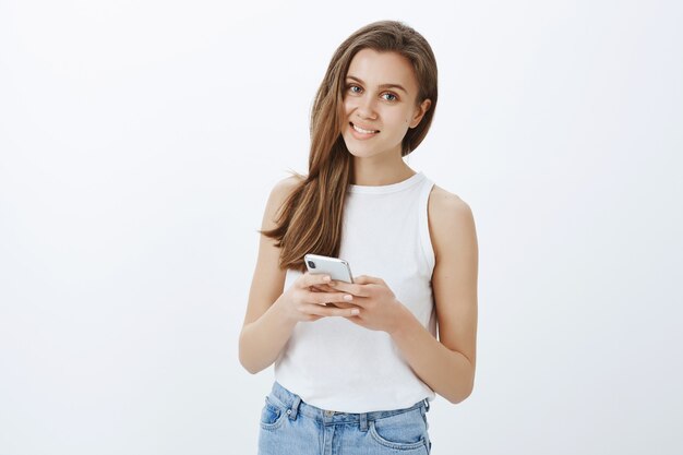 Portrait d'élégante jeune fille moderne à l'aide de smartphone et souriant heureux