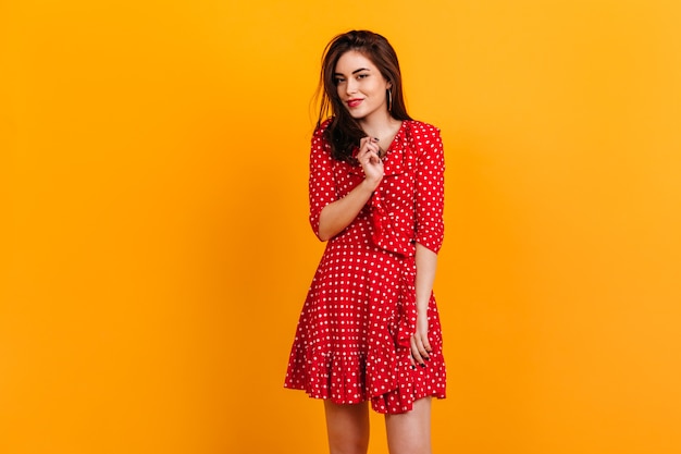 Portrait d'élégante jeune fille en robe rouge. Le modèle est mignon souriant sur le mur orange.