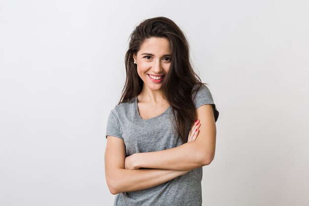 Portrait d'élégante jeune jolie femme souriante en t-shirt gris sur, isolé, look naturel, longs cheveux bruns, bras croisés