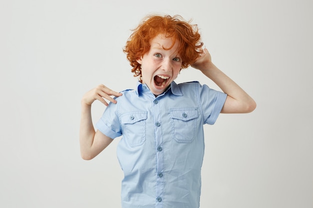 Portrait d'enfant fou de gingembre aux cheveux bouclés et taches de rousseur sautant, s'amusant avec la bouche ouverte et l'expression du visage fou.