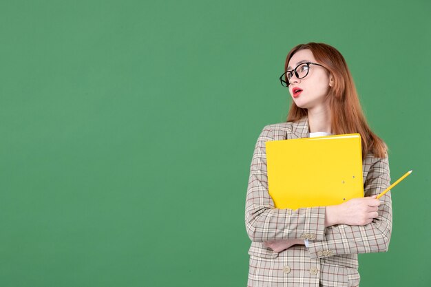 Portrait d'enseignante posant avec un fichier jaune et un crayon sur vert