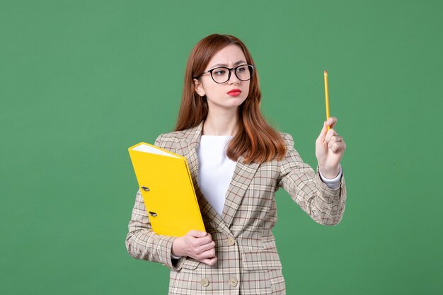 Portrait d'une enseignante tenant des fichiers jaunes et un crayon sur vert