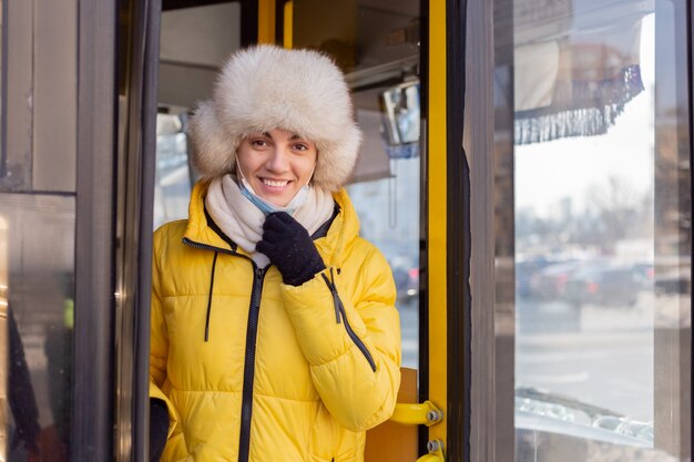 Portrait ensoleillé lumineux d'une jeune femme dans des vêtements chauds happy smiling descend du bus, enlève son masque de protection