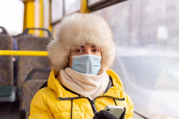 Portrait ensoleillé lumineux d'une jeune femme en vêtements chauds dans un bus de la ville par une journée d'hiver avec un téléphone portable à la main