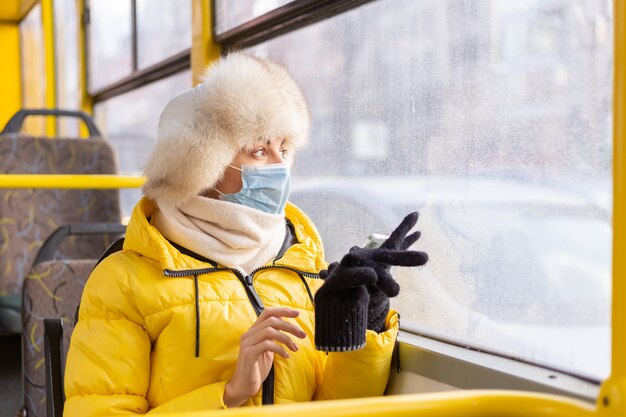 Portrait ensoleillé lumineux d'une jeune femme en vêtements chauds dans un bus de la ville par une journée d'hiver avec un téléphone portable à la main