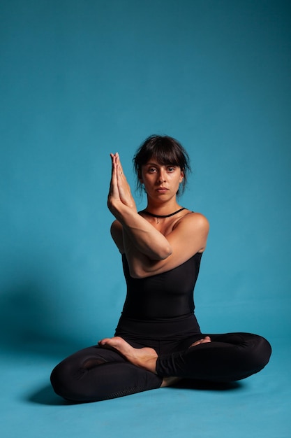 Portrait d'un entraîneur adulte souriant debout en position padmasana tenant les bras en position croisée pratiquant la méditation spirituelle. Personne athlétique travaillant à un mode de vie sain étirant les muscles du corps