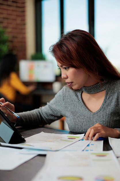 Portrait d'un entrepreneur asiatique analysant des graphiques marketing sur une tablette travaillant à la stratégie d'entreprise dans un bureau de démarrage. Femme directrice exécutive debout à table partenariat de planification