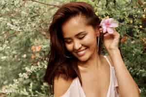 Photo gratuite portrait d'été de belle femme asiatique avec fleur dans les cheveux posant dans le jardin.