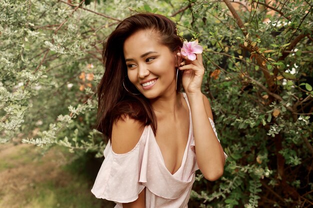 Portrait d'été de belle femme asiatique avec fleur dans les cheveux posant dans le jardin.