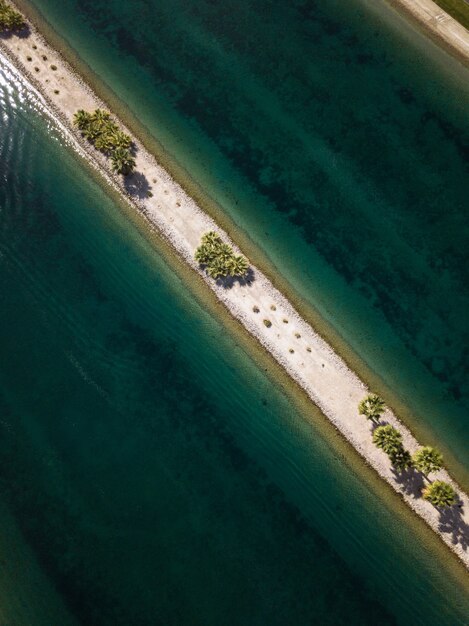 Portrait d'une étroite ligne de sable avec des arbres verts au milieu de la mer