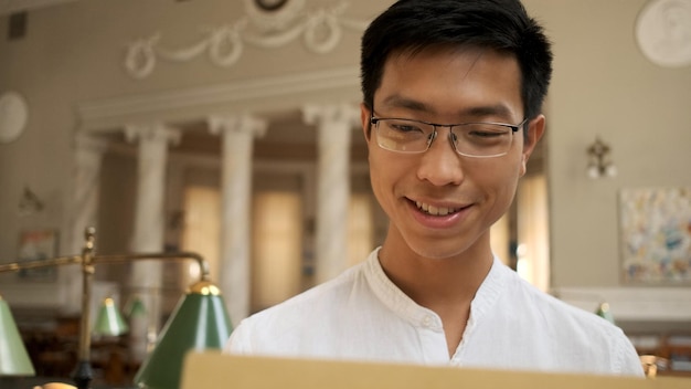 Portrait d'un étudiant asiatique souriant ouvrant joyeusement une enveloppe avec les résultats des examens dans la bibliothèque universitaire