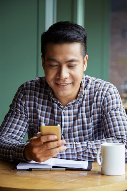 Portrait d'un étudiant asiatique surfer sur le net sur smartphone dans la coffee shop