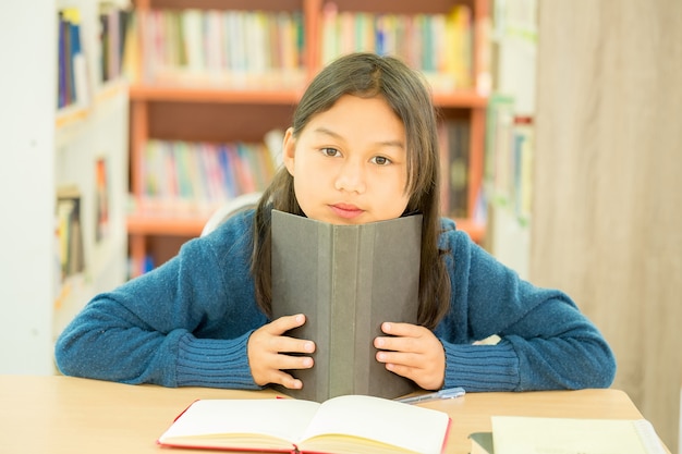 Portrait d'un étudiant intelligent avec un livre ouvert en le lisant dans une bibliothèque universitaire