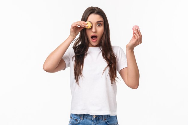 Portrait expressif jeune femme tenant deux macarons savoureux sur les yeux