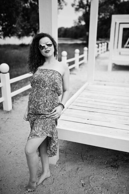 Portrait d'une fabuleuse jeune fille portant une tenue chic posant sur une terrasse en bois blanc Photo noir et blanc