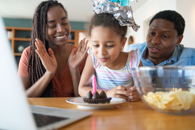 Portrait d'une famille célébrant son anniversaire en ligne lors d'un appel vidéo avec un ordinateur portable tout en restant à la maison