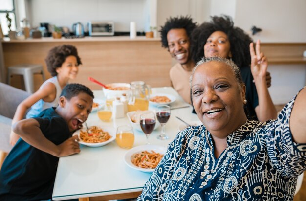 Portrait de famille multigénérationnelle afro-américaine prenant un selfie ensemble tout en dînant à la maison.