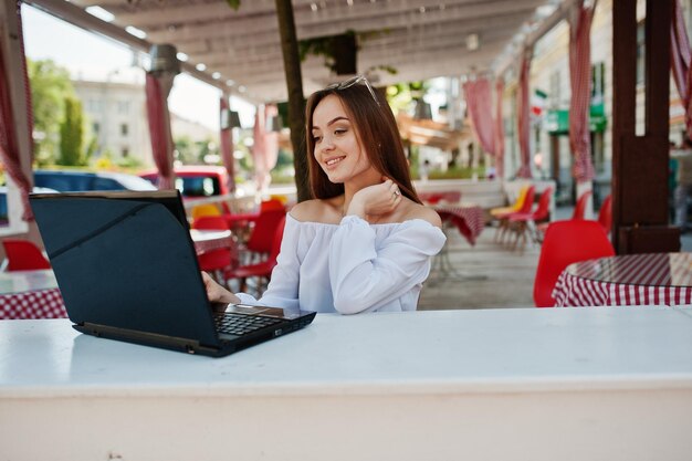 Portrait d'une femme d'affaires prospère et indépendante portant des vêtements décontractés intelligents et des lunettes travaillant sur un ordinateur portable dans un café