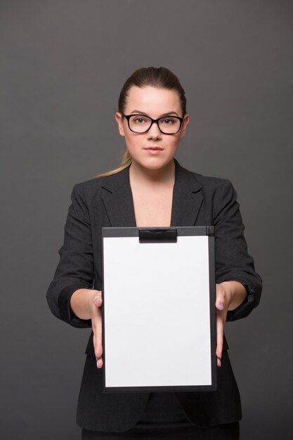 Portrait d'une femme d'affaires sérieuse tenant un presse-papiers devant elle avec une page vierge. Jolie dame à lunettes posant en tailleur noir.