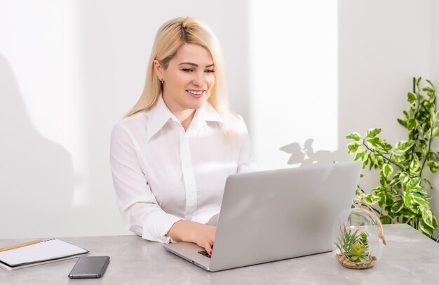 Portrait d'une femme d'affaires sérieuse utilisant un ordinateur portable au bureau contre un mur blanc