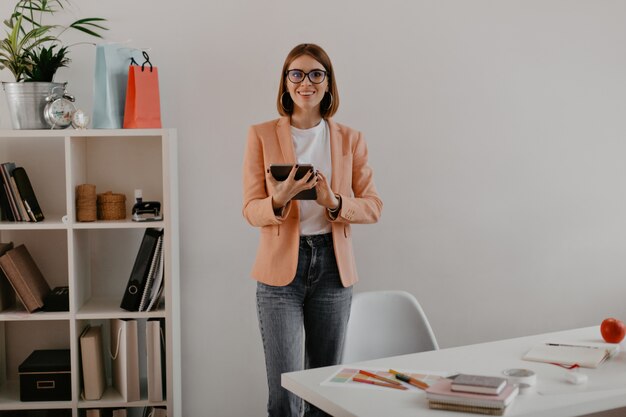 Portrait de femme d'affaires souriante en veste de couleur pêche au bureau blanc.