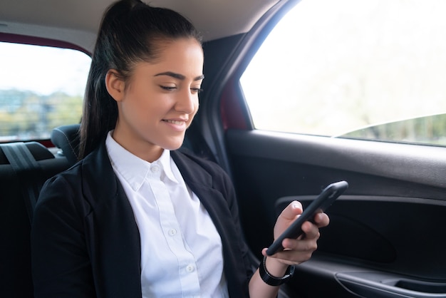 Portrait d'une femme d'affaires utilisant son téléphone portable sur le chemin du travail dans une voiture