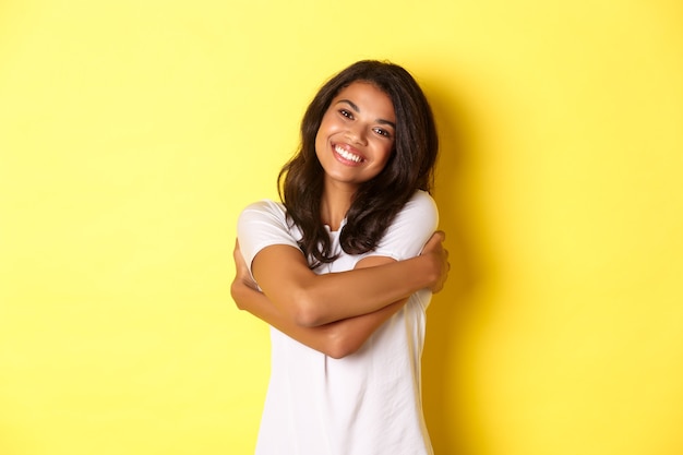 Portrait d'une femme afro-américaine joyeuse s'embrassant et souriante heureuse debout sur du jaune