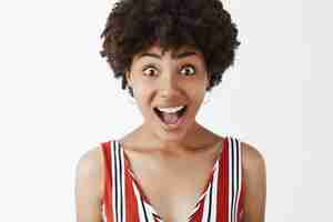 Photo gratuite portrait de femme afro-américaine ravie et charmée avec coupe de cheveux afro, haletant de bonheur, souriant largement et regardant amusé, écoutant attentivement