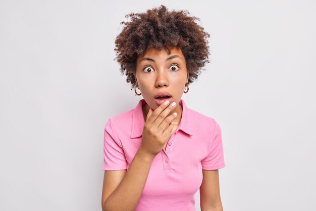 Le portrait d'une femme afro-américaine surprise haletant d'émerveillement et regarde sans voix de crainte et d'incrédulité ne peut pas croire que ses yeux portent un t-shirt décontracté isolé sur un mur blanc