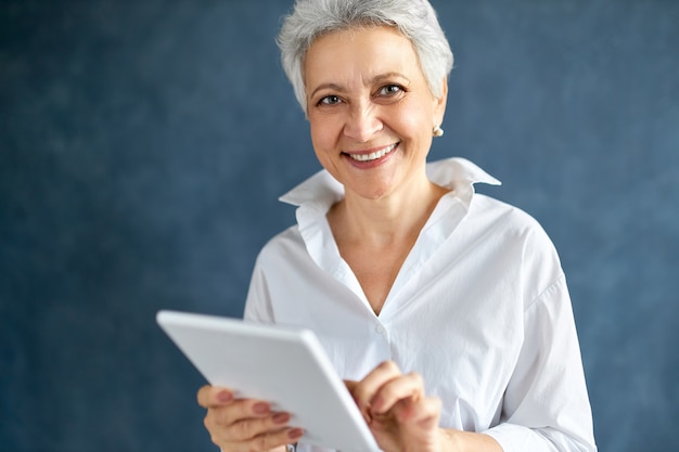 Portrait de femme d'âge moyen aux cheveux gris travaillant à distance à l'aide d'une connexion sans fil sur tablette numérique