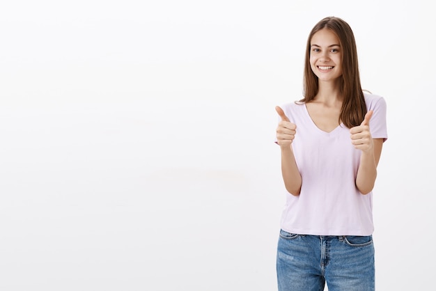 Portrait de femme amicale heureuse et heureuse satisfaite en chemisier décontracté et jeans montrant les pouces vers le haut et souriant largement satisfait de la bonne qualité du produit