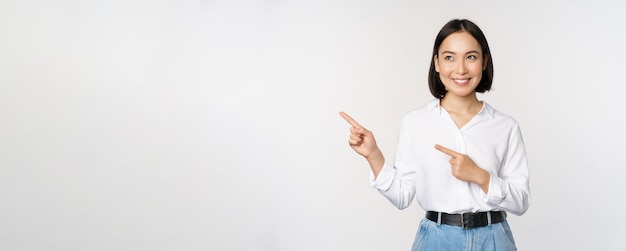 Portrait d'une femme asiatique adulte séduisante pointant vers la gauche avec un sourire heureux montrant une bannière ou