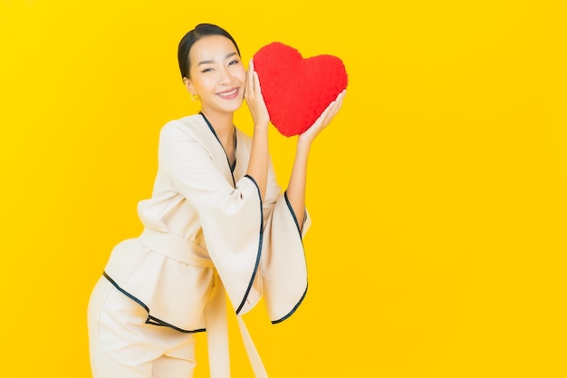 Portrait de femme asiatique belle jeune entreprise avec oreiller en forme de coeur sur le mur de couleur jaune