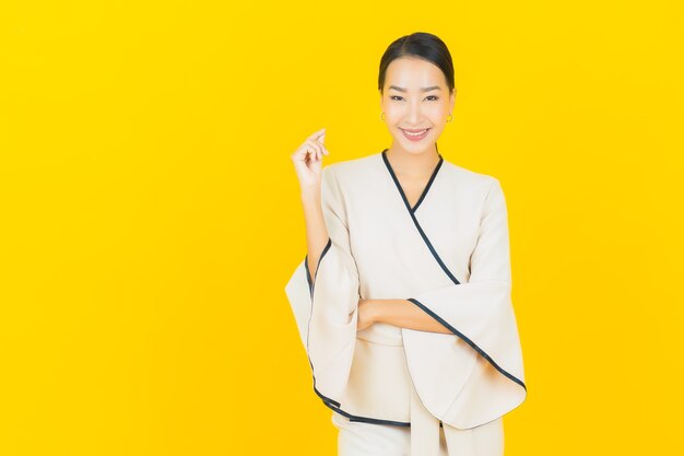 Portrait de femme asiatique belle jeune entreprise souriant avec costume blanc sur mur jaune