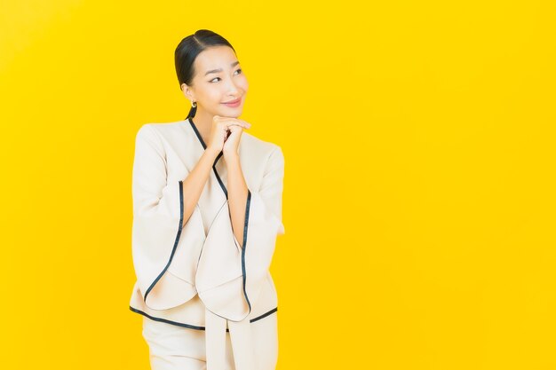 Portrait de femme asiatique belle jeune entreprise souriant avec costume blanc sur mur jaune