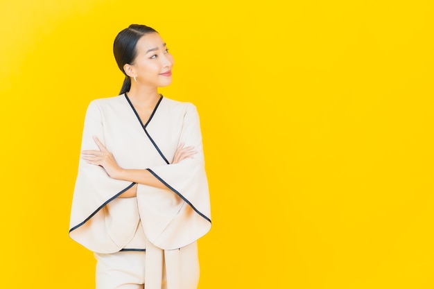 Portrait de femme asiatique belle jeune entreprise souriant avec costume blanc sur mur jaune