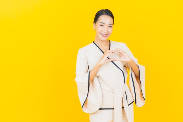 Portrait de femme asiatique belle jeune entreprise souriant avec costume blanc sur mur jaune