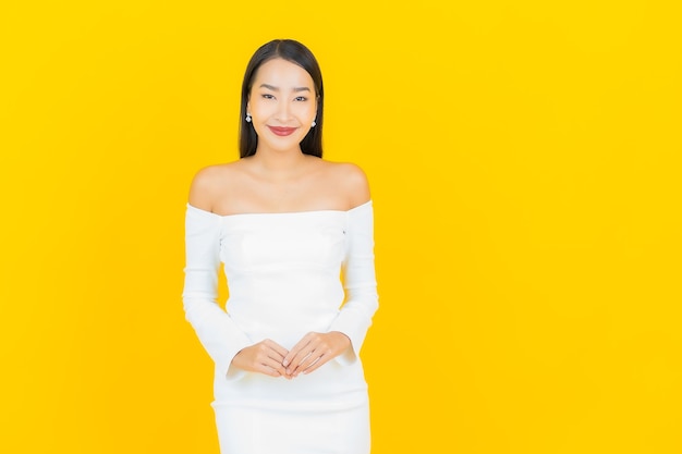 Portrait de femme asiatique belle jeune entreprise souriant avec une robe blanche sur un mur jaune