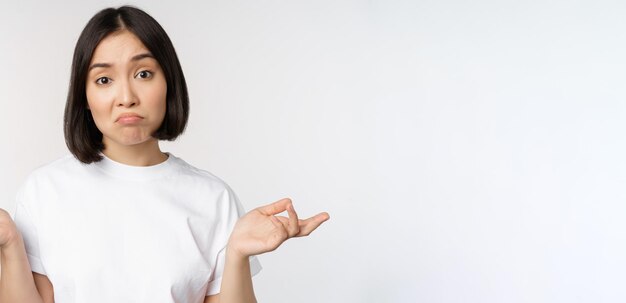 Portrait d'une femme asiatique confuse, haussant les épaules, l'air perplexe, perplexe, debout sur fond blanc Copier l'espace