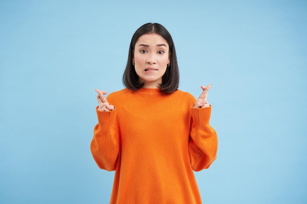 Photo gratuite portrait de femme asiatique croiser les doigts espère et prie pour quelque chose fait un souhait se dresse sur bleu ba