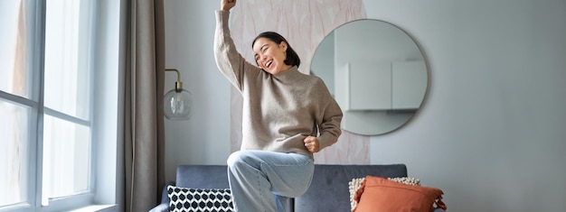 Photo gratuite portrait d'une femme asiatique heureuse dansant en se réjouissant et en triomphant, se sentant optimiste à la maison